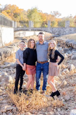 Family of four stands together on rocky terrain with bridge in background during autumn in Springfield, MO.