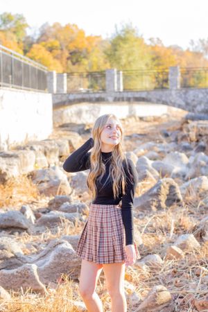 Person in black sweater and plaid skirt poses near bridge during golden hour in Springfield, MO.