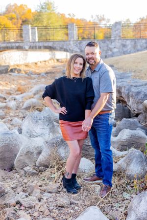 Couple poses together on rocky terrain with metal bridge visible in background in Springfield, MO.
