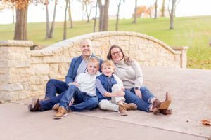 Family in coordinating blue outfits relaxes together against stone wall outdoors in Springfield, MO.