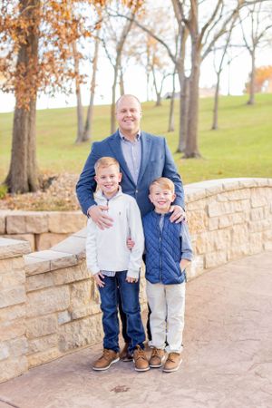 A man in a blue blazer stands with two children on a stone path surrounded by autumn trees in Springfield, MO.