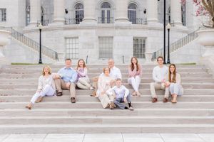 Family group seated on white stone steps wearing coordinated light colored outfits.