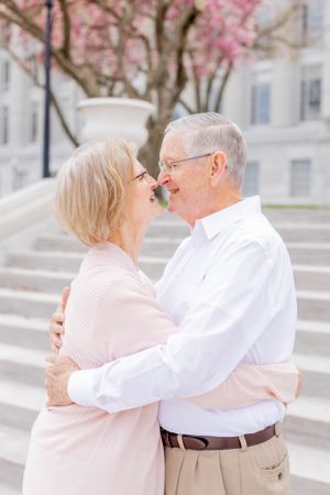 Elderly couple embraces tenderly in front of stone stairs with blooming cherry blossoms in spring.