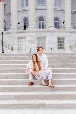 Couple sits together on elegant stone staircase of classical building.
