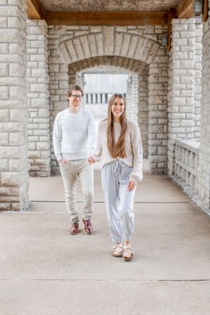 Couple walking through stone archway in matching neutral colored outfits.
