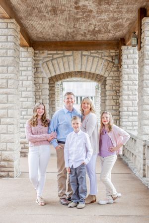 Family portrait under stone archway wearing coordinated pastel outfits.
