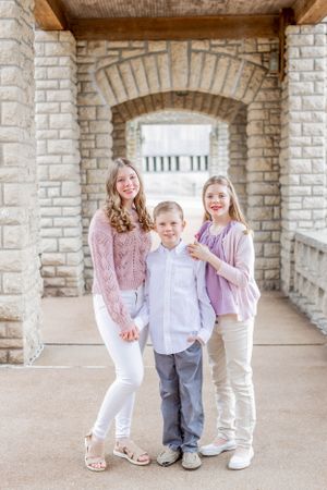 Group portrait of three people under stone archway in light colored clothing.
