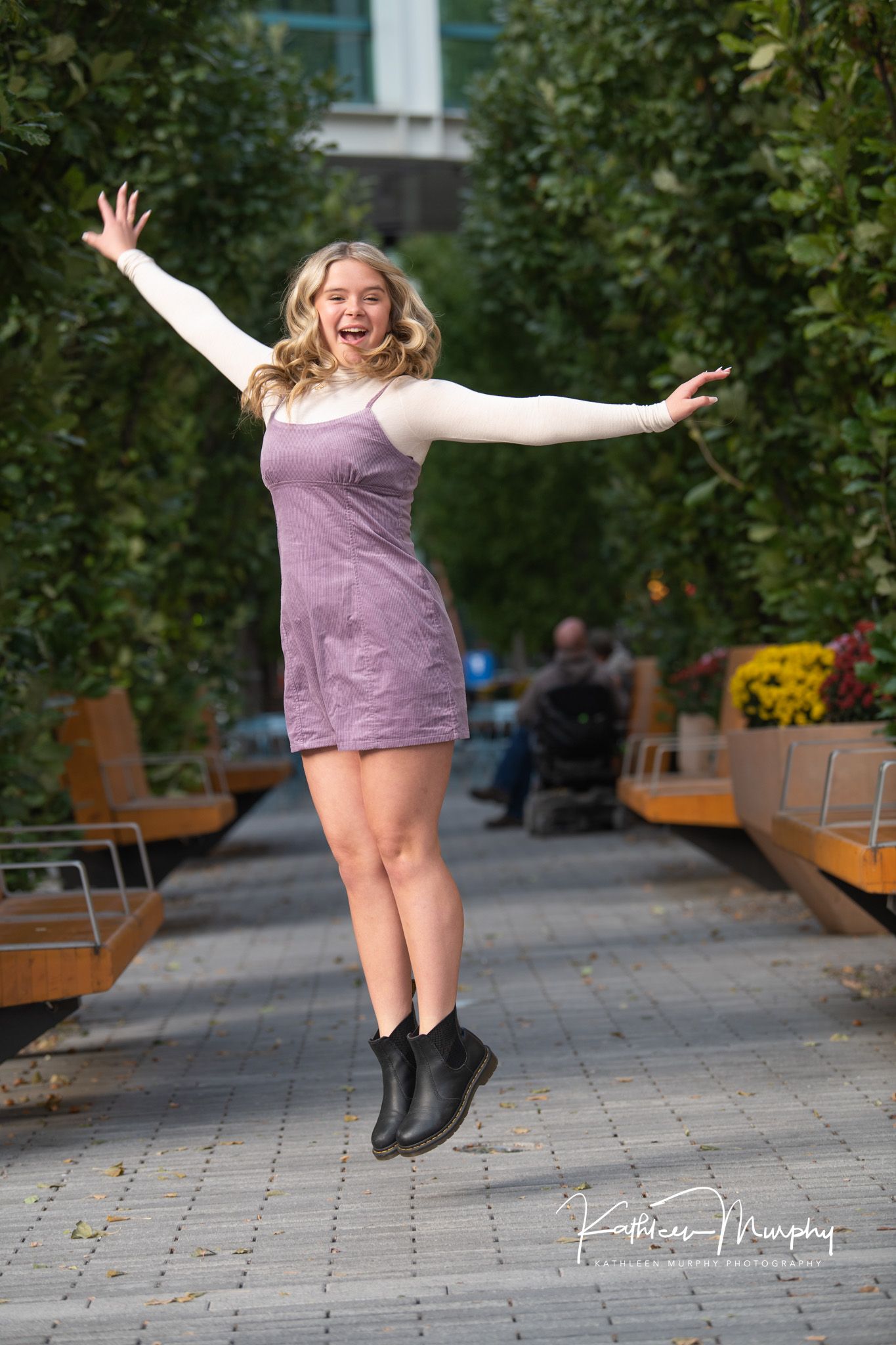 Person in purple dress jumping joyfully on urban walkway.