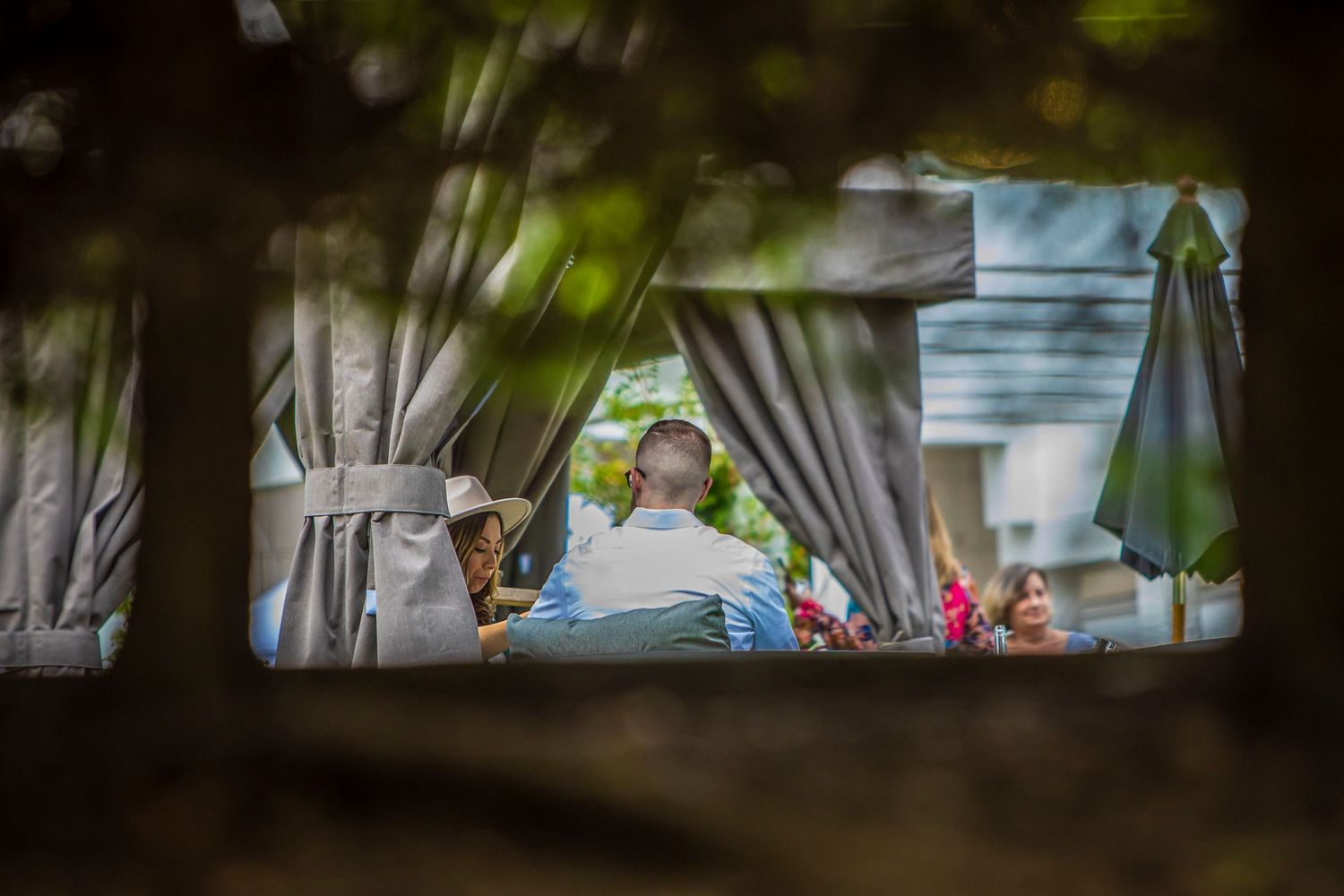 a couple having wine with the picture taken through a bush