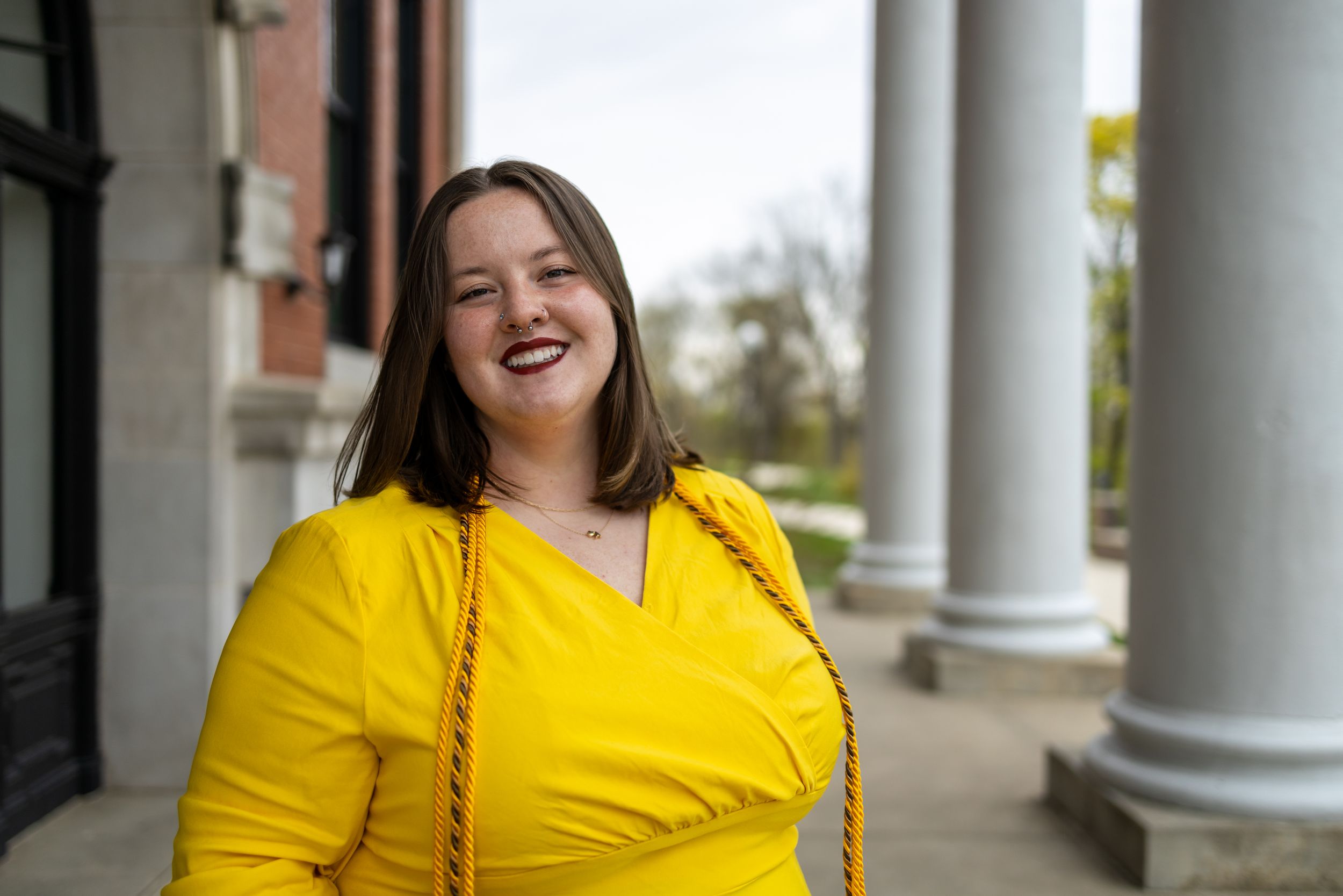 A person in yellow dress smiling brightly between classic white columns.