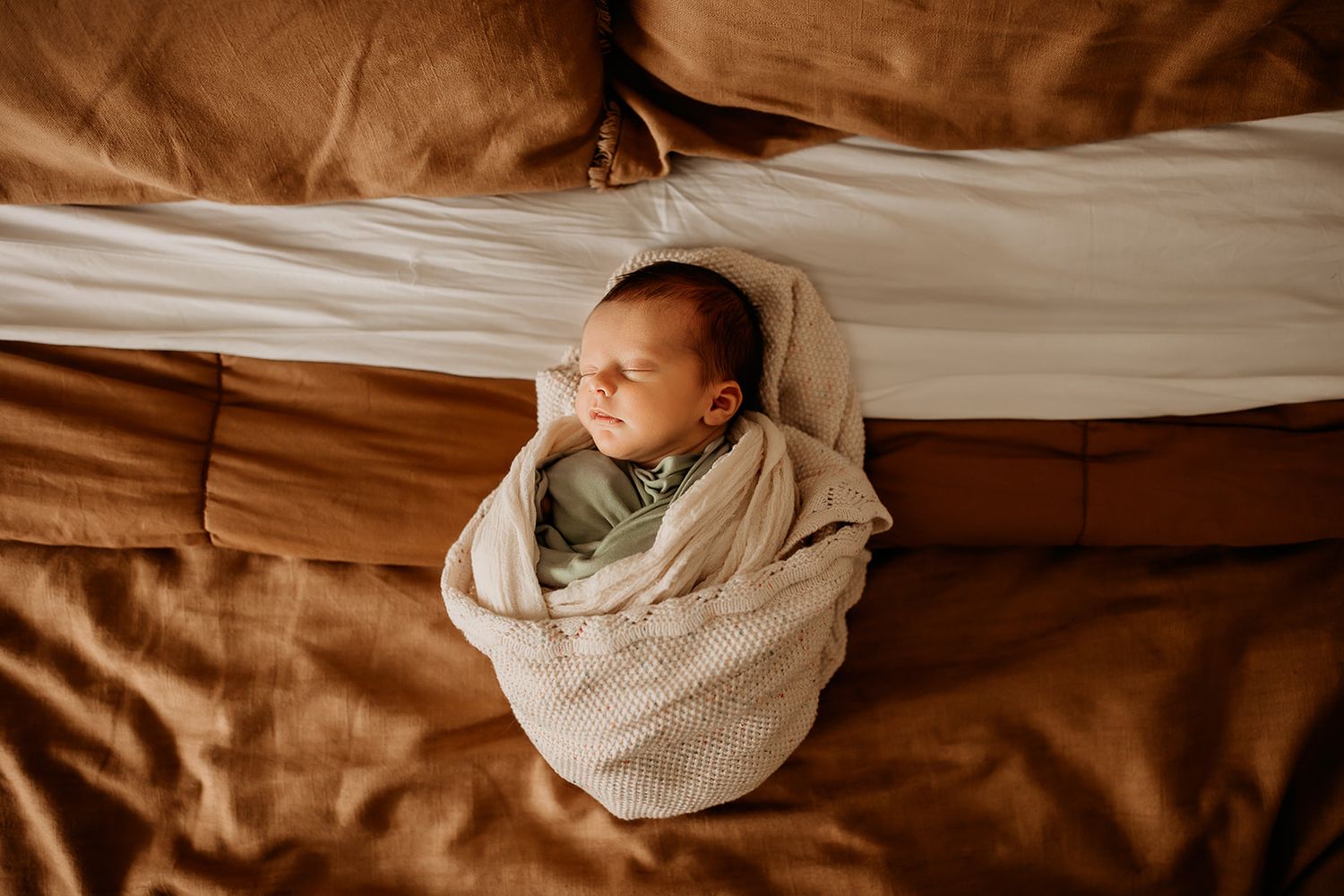 A swaddled newborn boy sleeps on his parents bed.