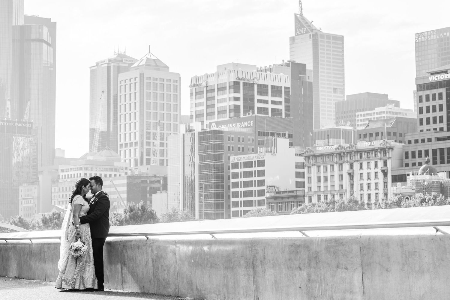 A couple embraces on a rooftop overlooking a cityscape in black and white.