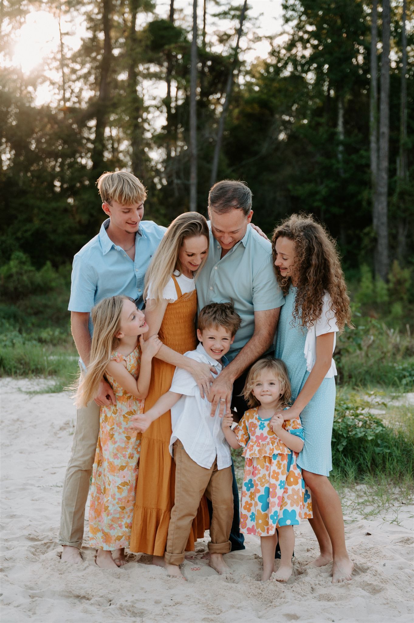 Group photo of family members huddled close together on sandy path with pine forest background.