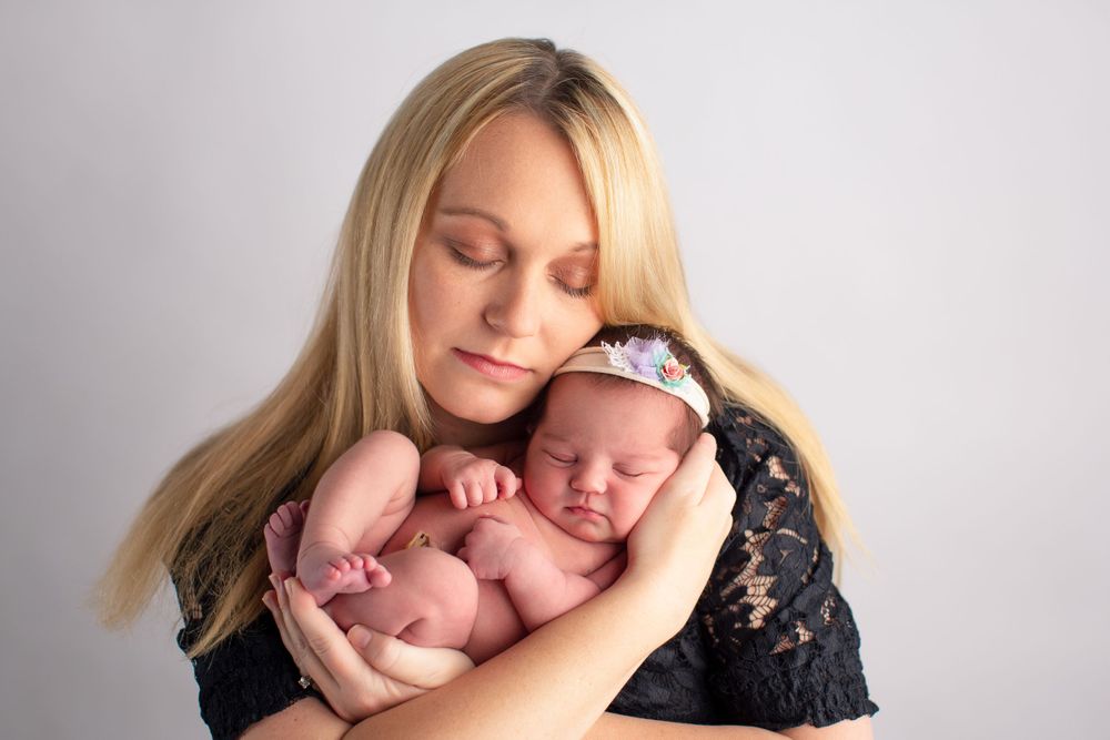 Tender moment of motherly embrace during newborn photo session on white background.