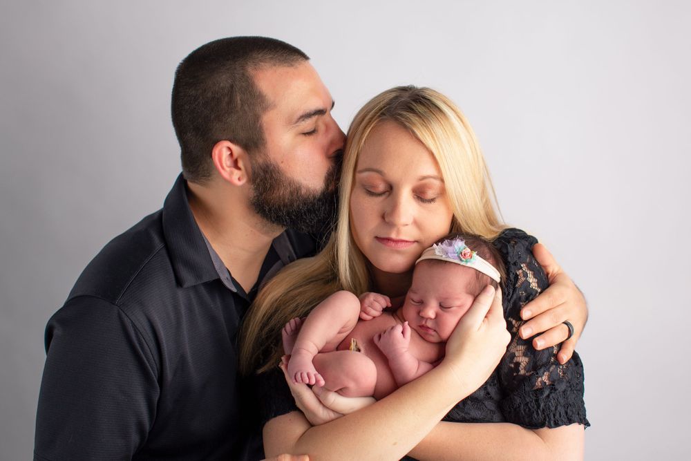 Intimate family portrait during newborn photo session against light gray background.