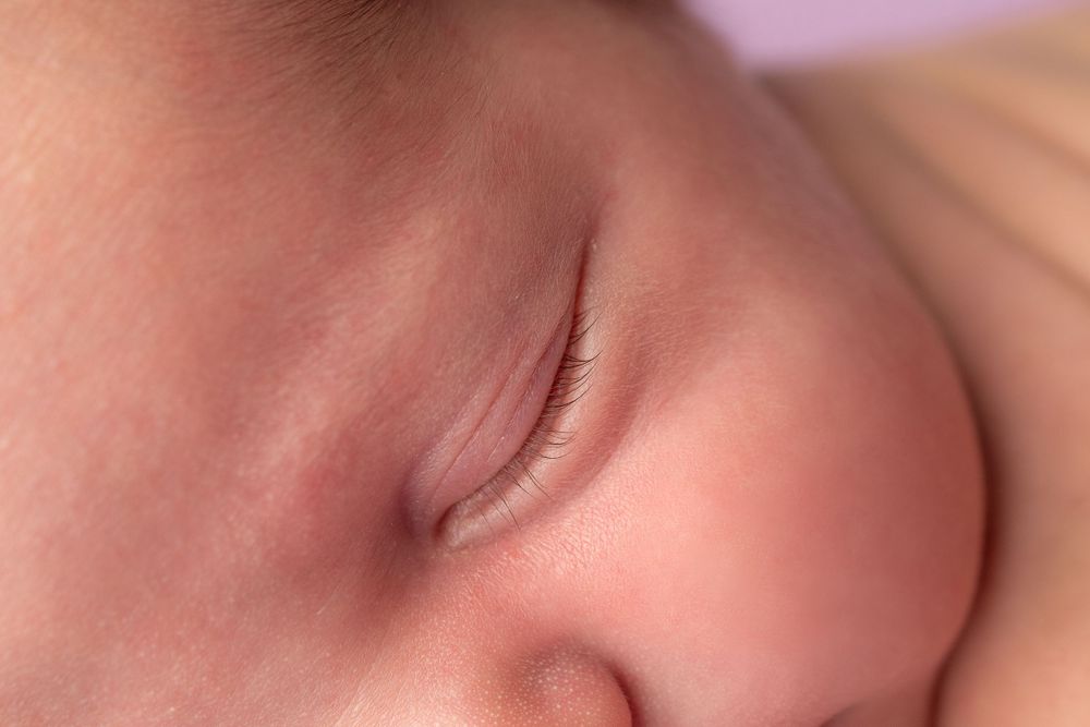 Close-up macro shot of sleeping baby's peaceful expression against purple background.