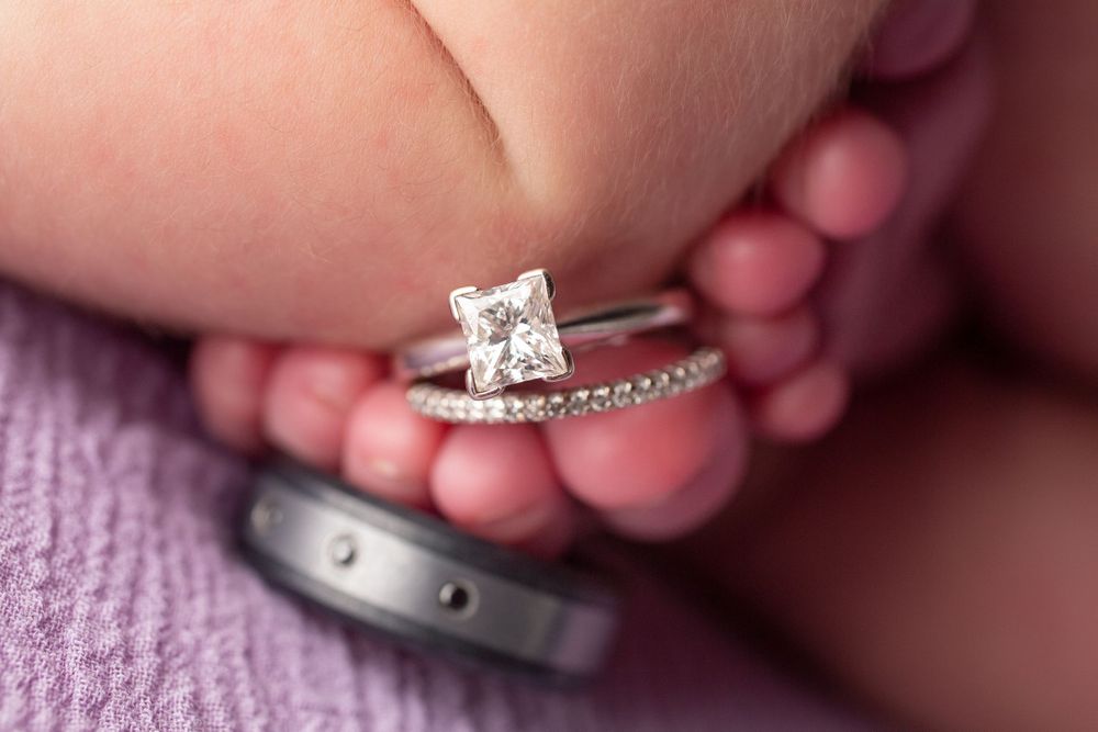 Wedding rings placed on tiny newborn feet against purple textile background.