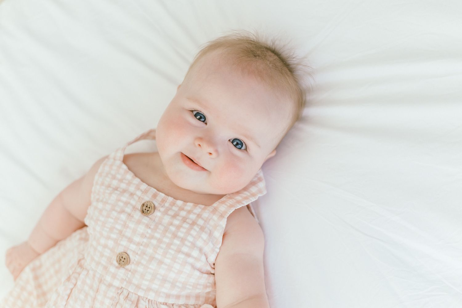 Baby in pink outfit lies on white bedding during newborn photography session.