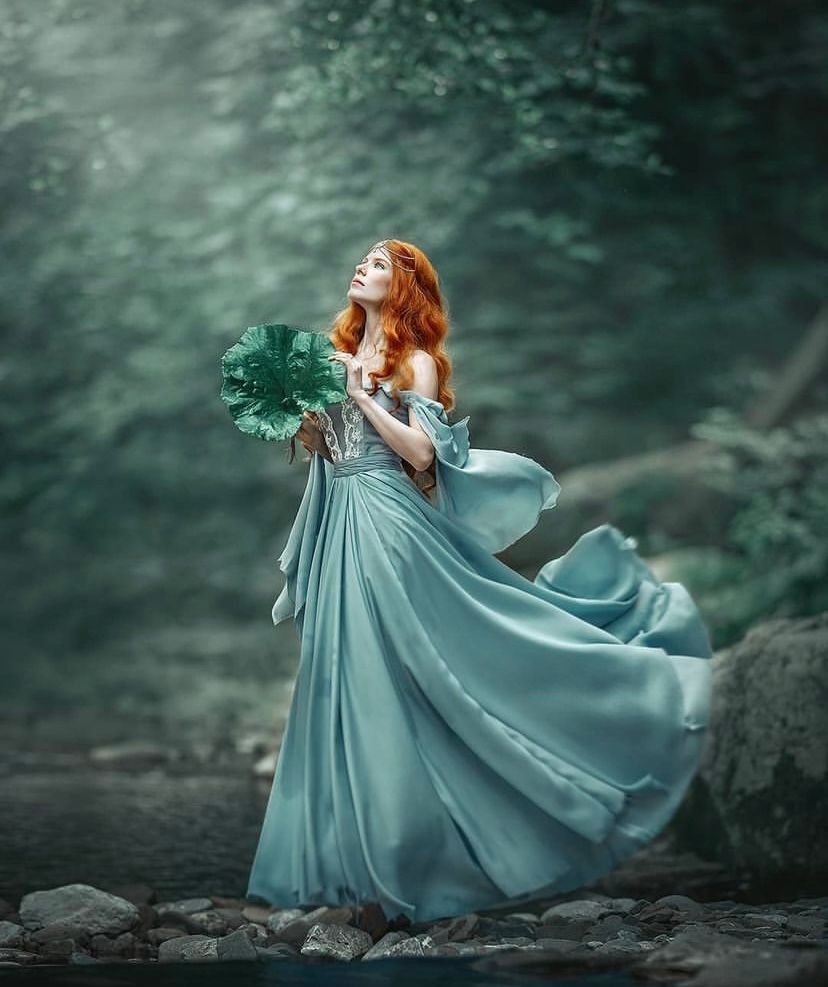 Ethereal fantasy portrait of woman in flowing teal dress against misty forest backdrop.