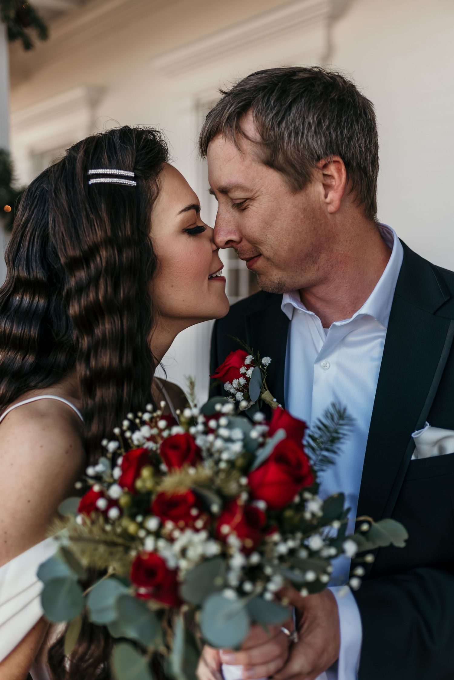 A romantic moment between newlyweds sharing an intimate pose with a red rose bouquet.