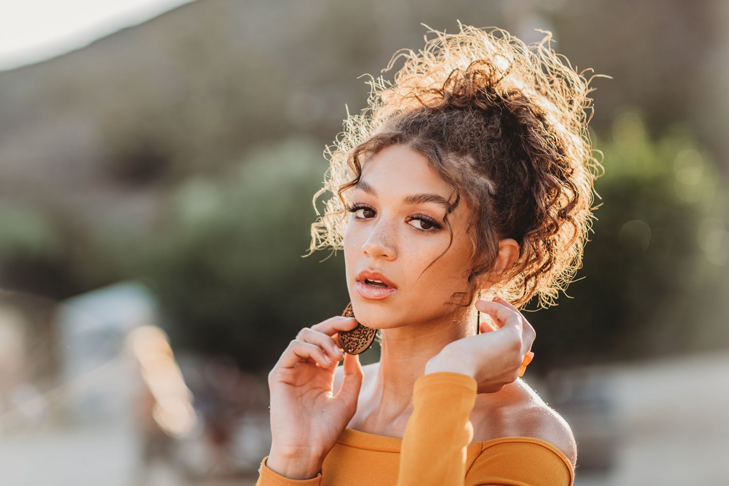 Natural light portrait with golden sunlit curls and soft bokeh background.
