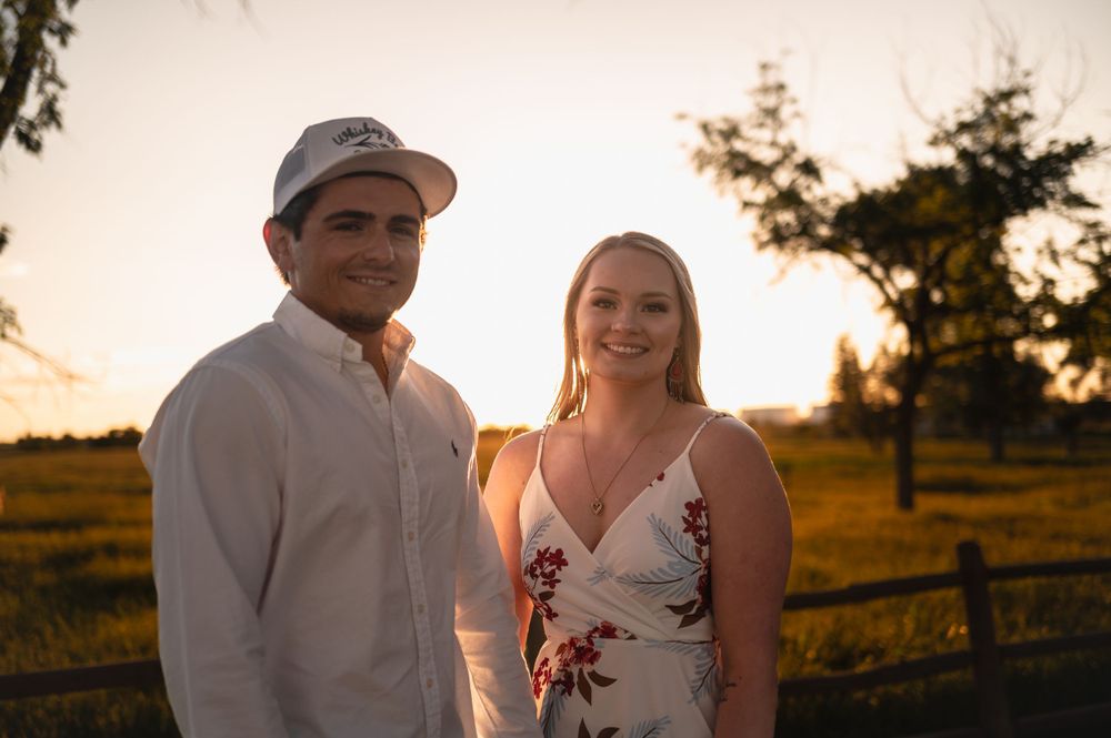 A couple stands together in a golden field at sunset wearing casual summer attire.