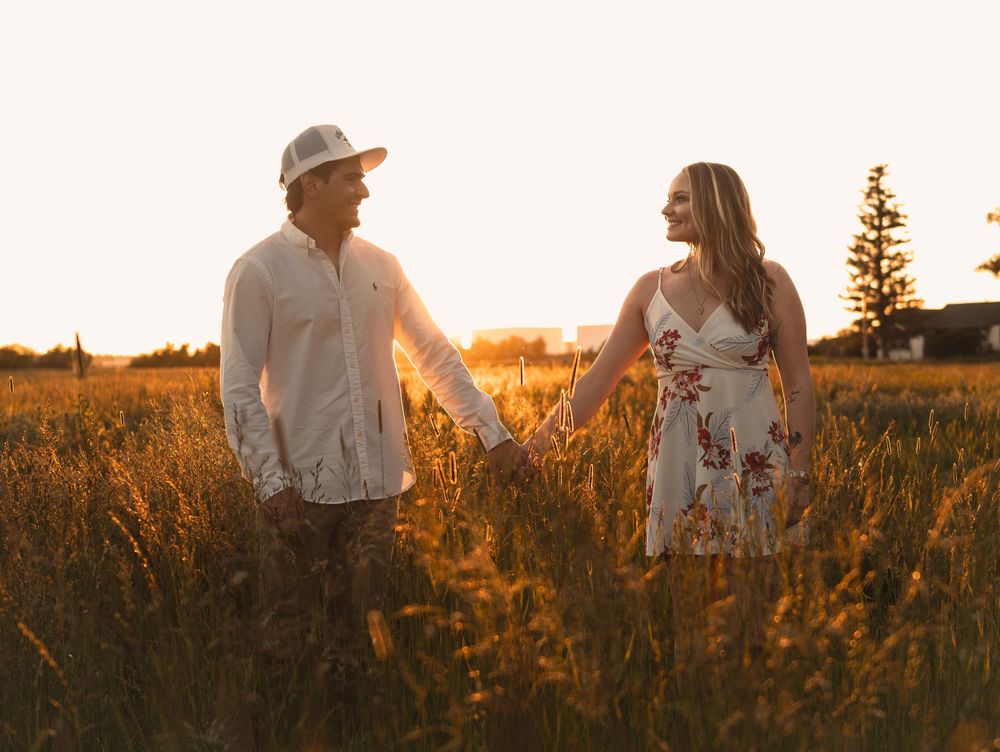 A couple walks hand in hand through a sun-drenched field at golden hour.