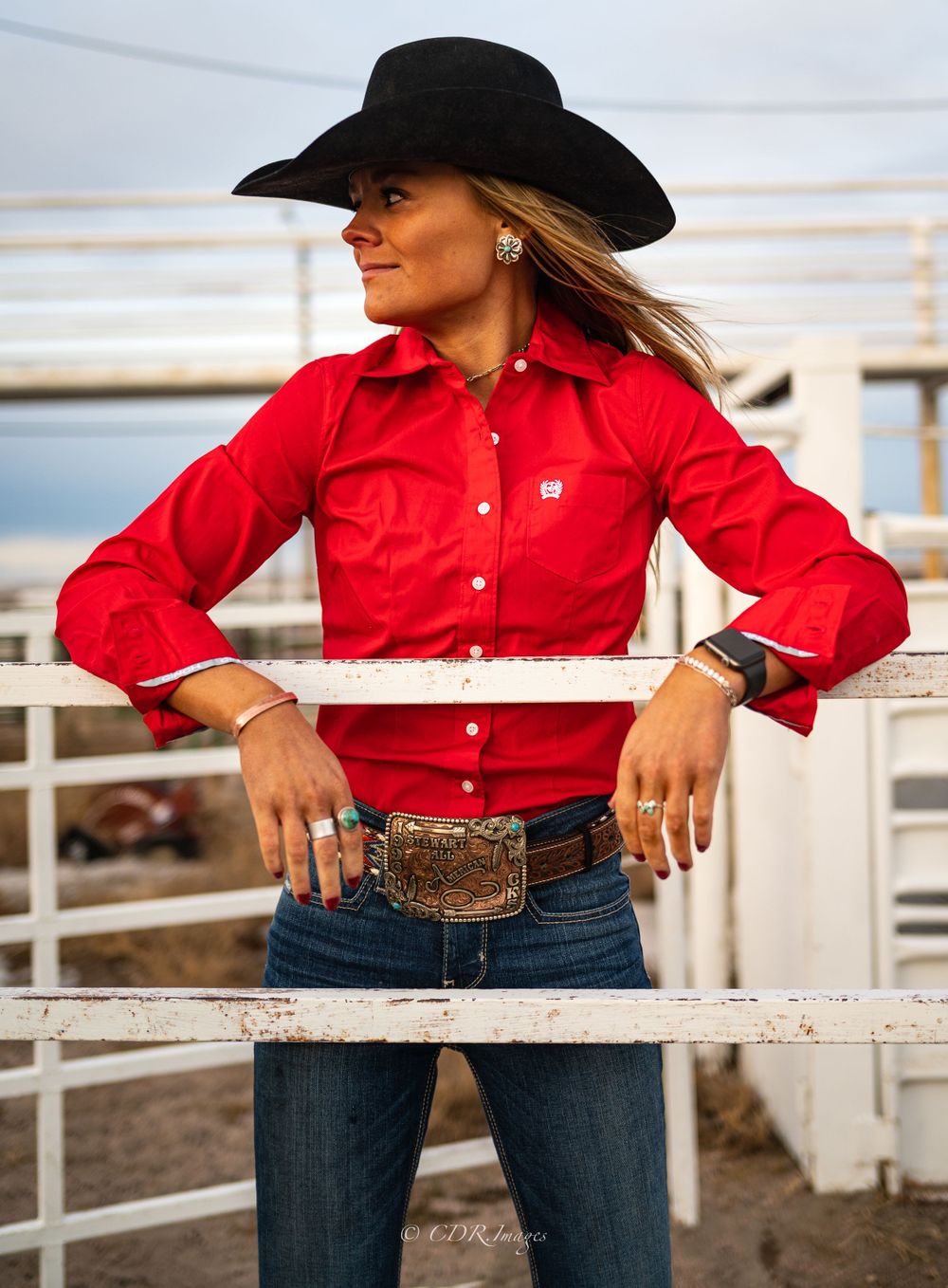Western style portrait with black cowboy hat and red shirt against white ranch fence.