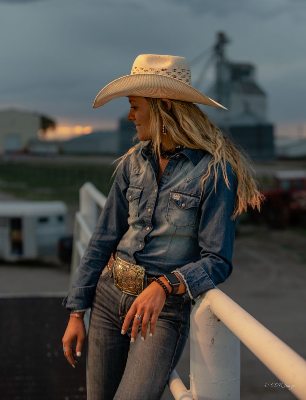 Rustic western scene with denim jacket and cowboy hat against grain silo at dusk.