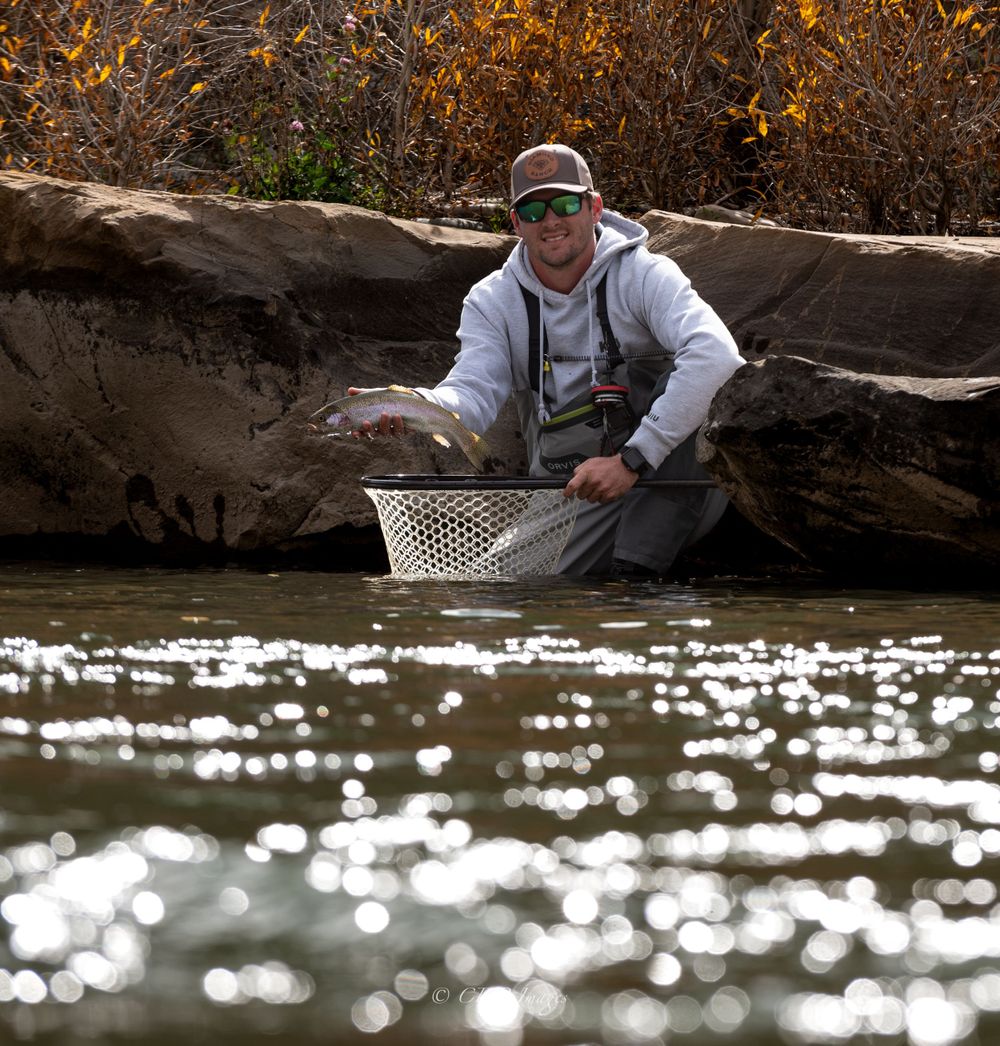 Fly fisherman in waders holding a fishing net in autumn river setting.