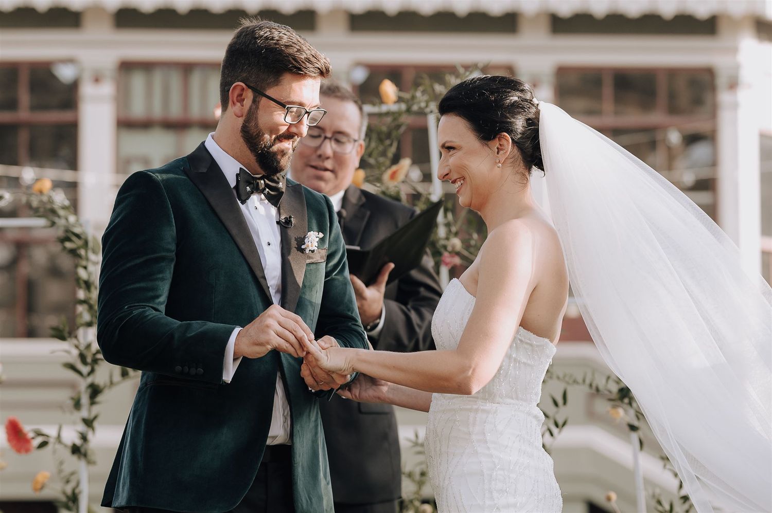 Wedding ceremony exchange of rings in front of Spanish colonial architecture.