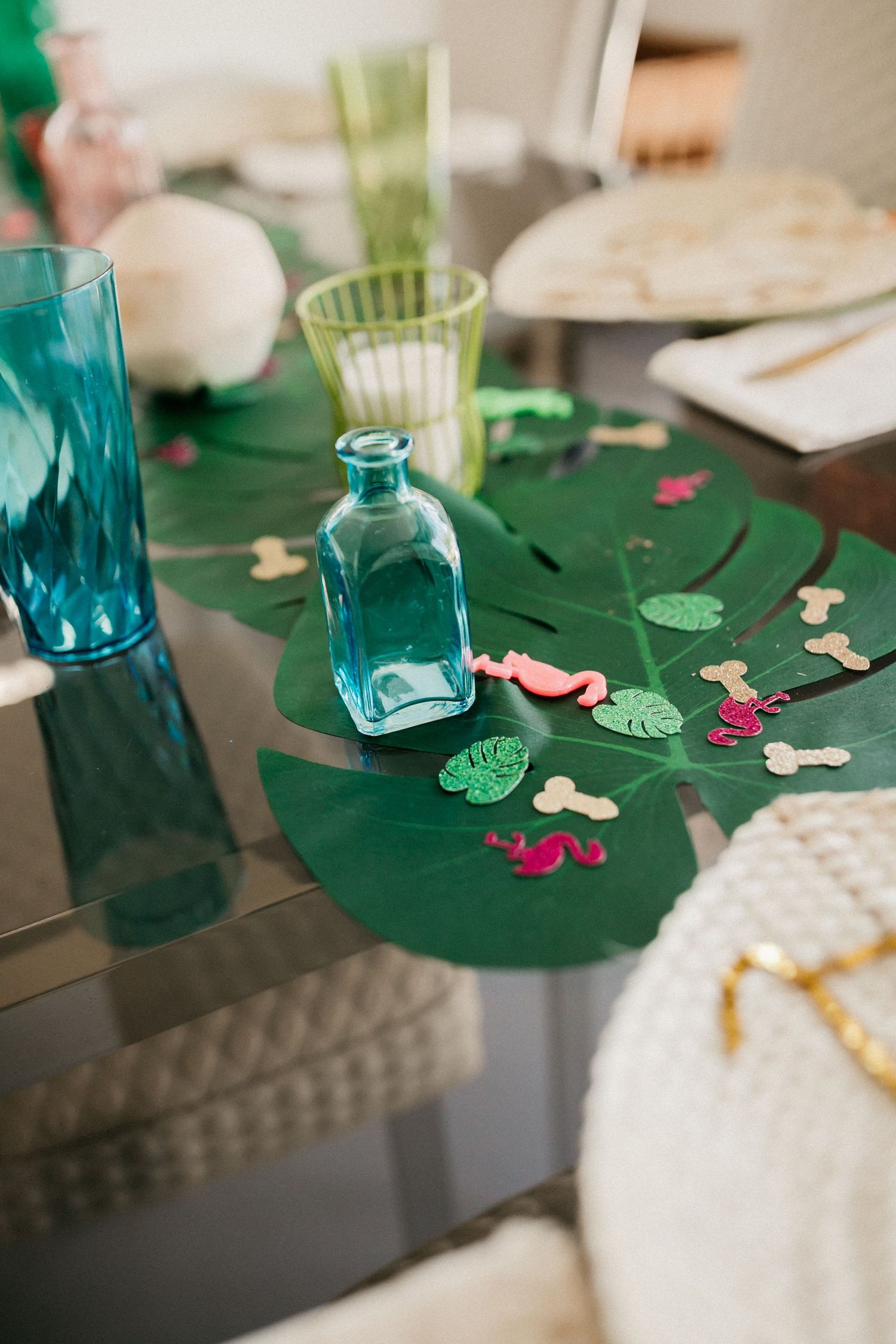 Party table decorated with green palm leaves, turquoise glassware, and scattered flower petals.