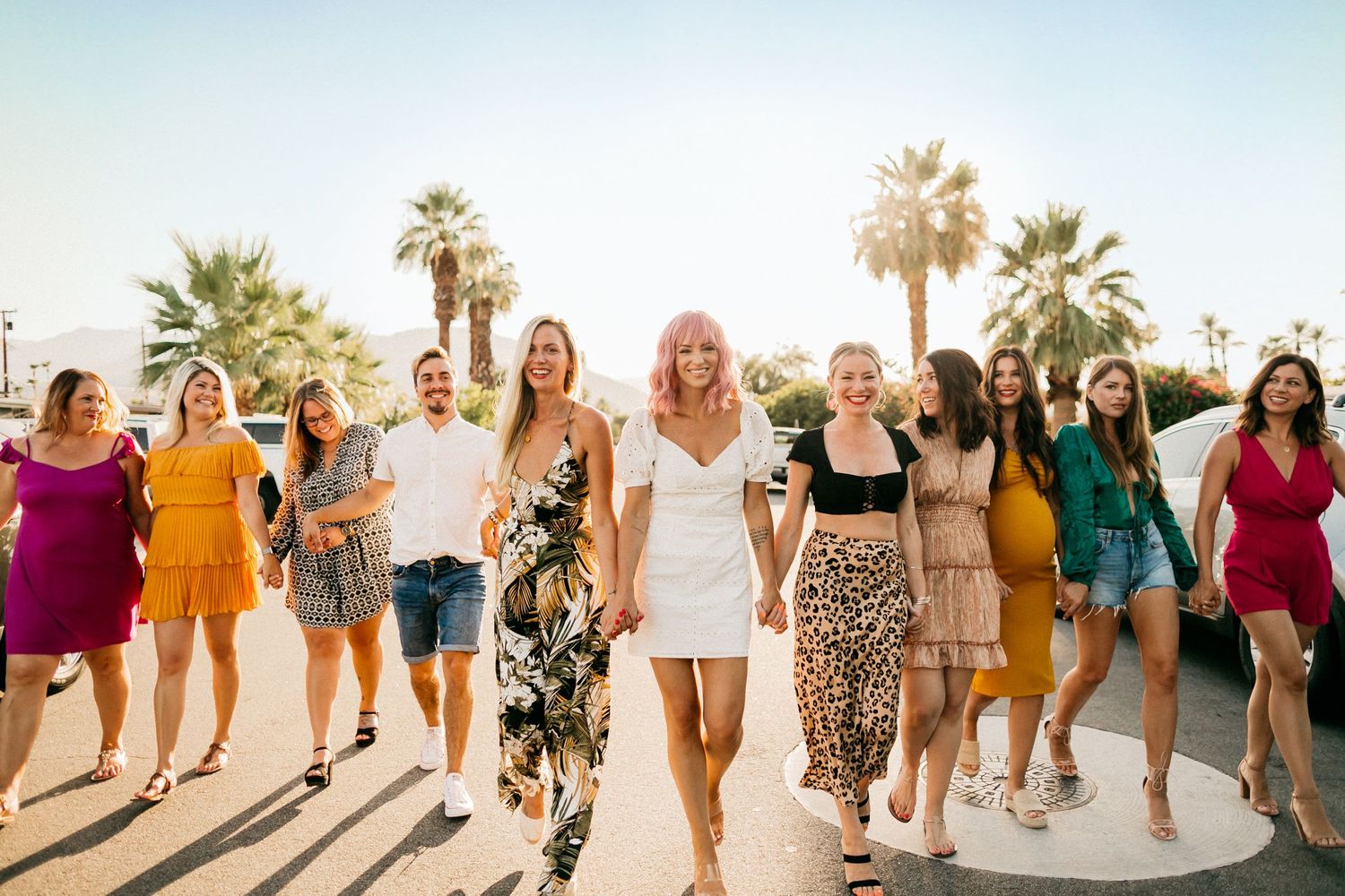 A group walking together in colorful outfits against a palm tree backdrop.