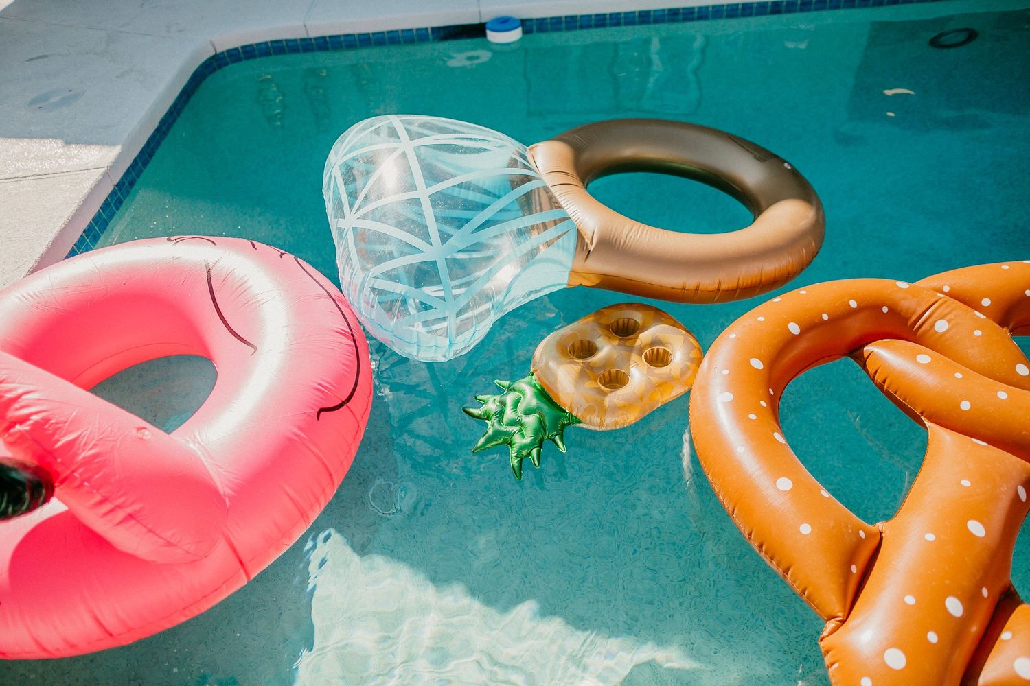 Pool floats including a pink flamingo and pretzel shape floating in turquoise water.