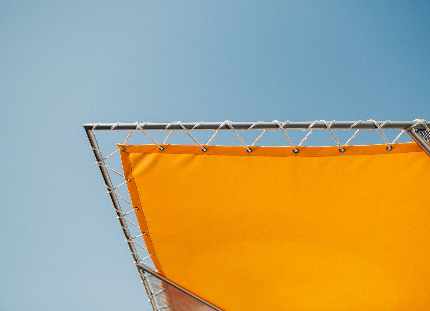 Orange fabric canopy against bright blue sky creating geometric shapes and shadows.