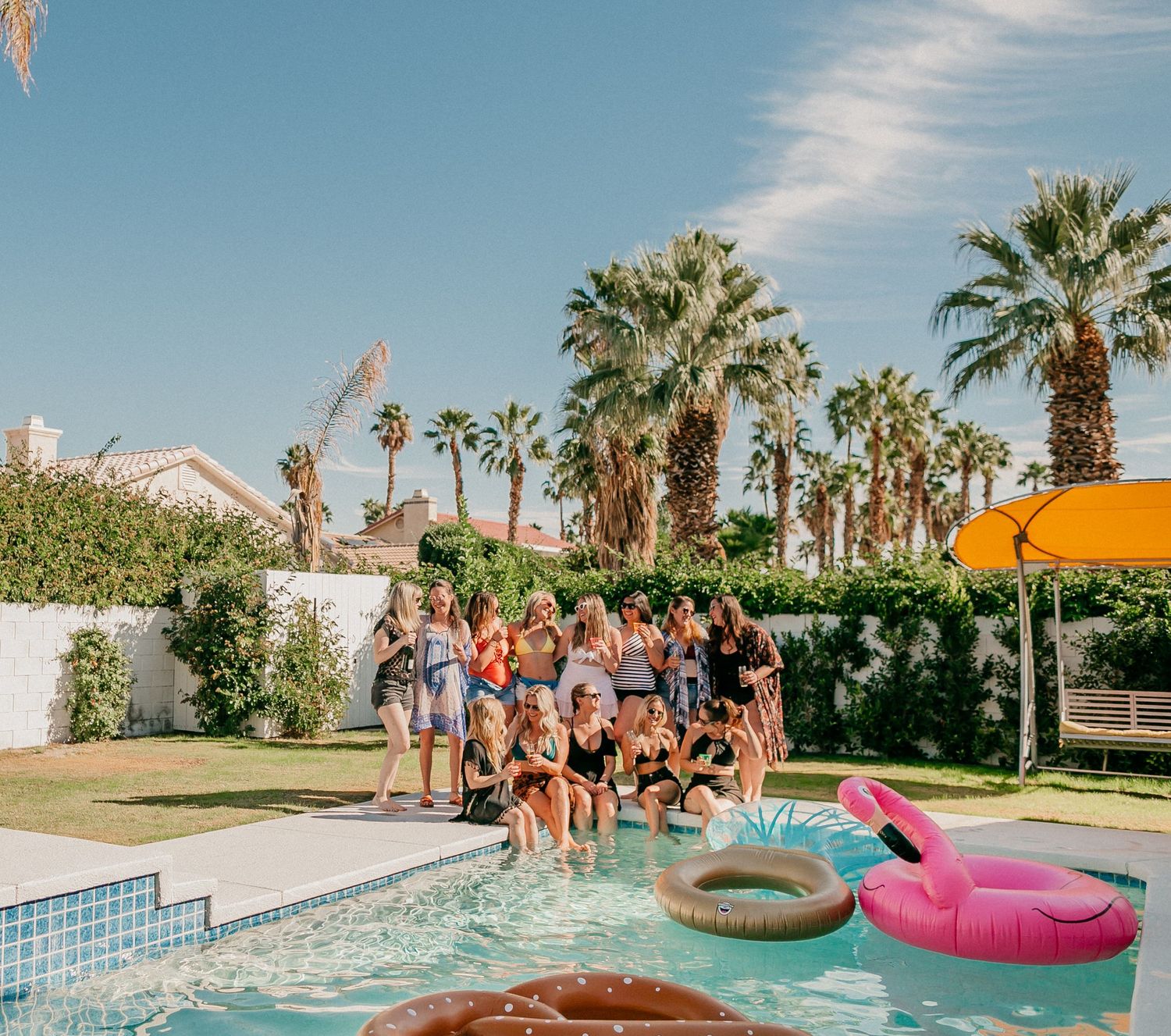 Palm tree lined pool party with colorful floats on a sunny day.