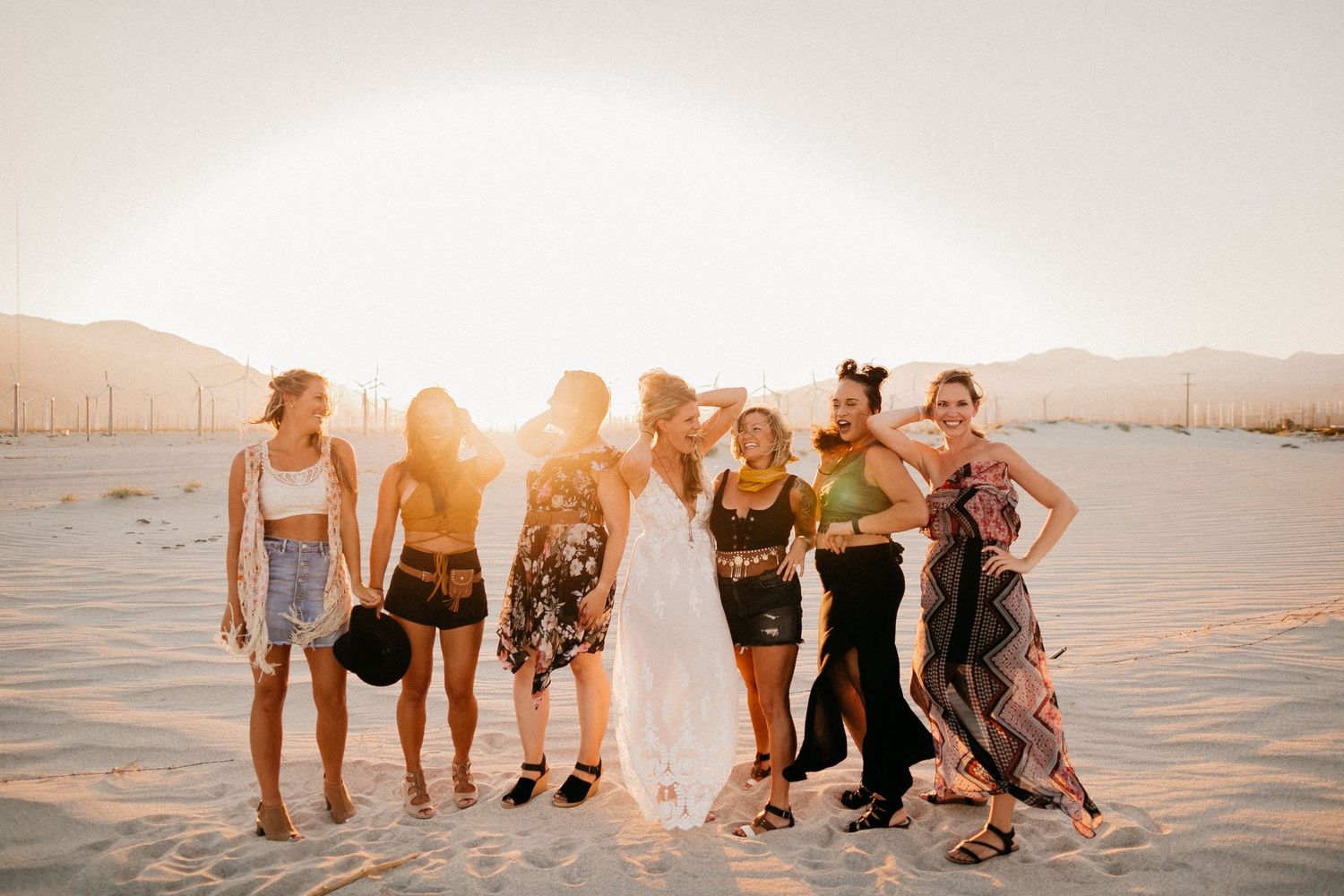 Wedding party posing together on beach at sunset with mountains in background.