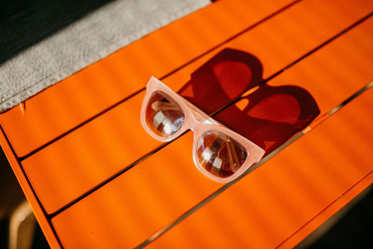 Heart-shaped sunglasses on vibrant orange striped surface in sunlight.