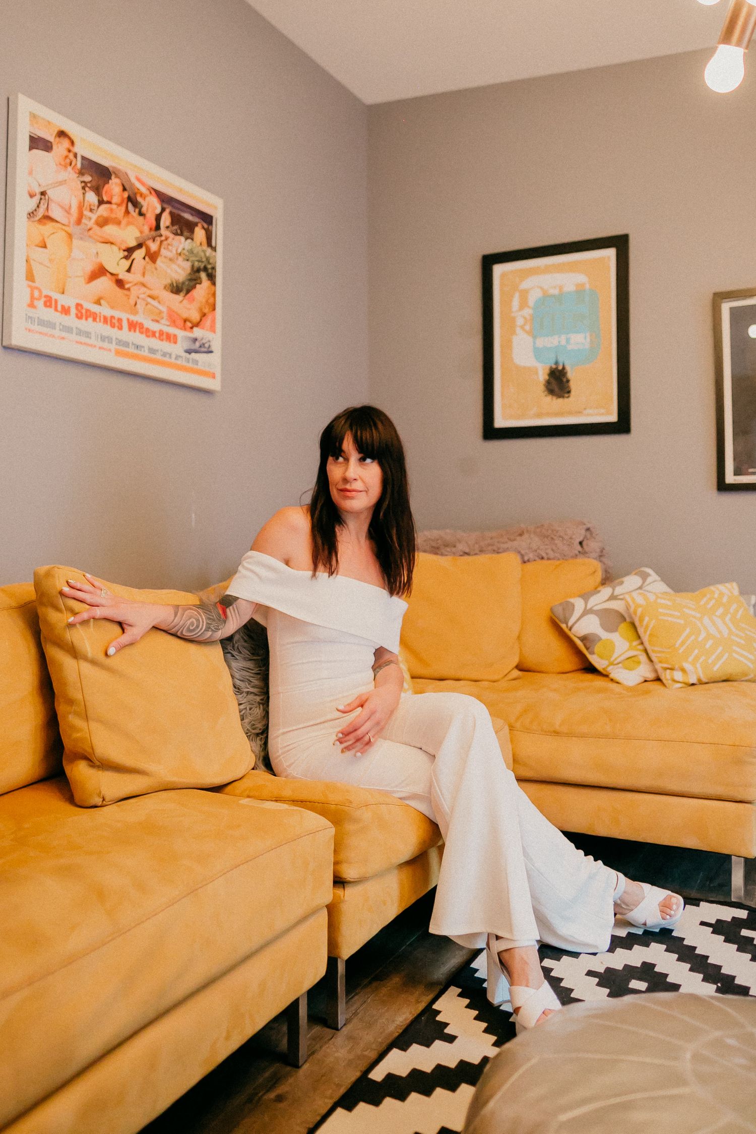 Woman in white dress relaxing on yellow sectional sofa in living room with framed wall art.