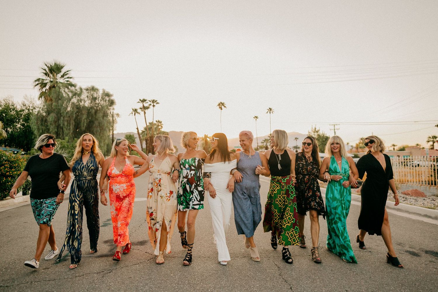 Group of wedding party guests walking together at sunset against palm trees.