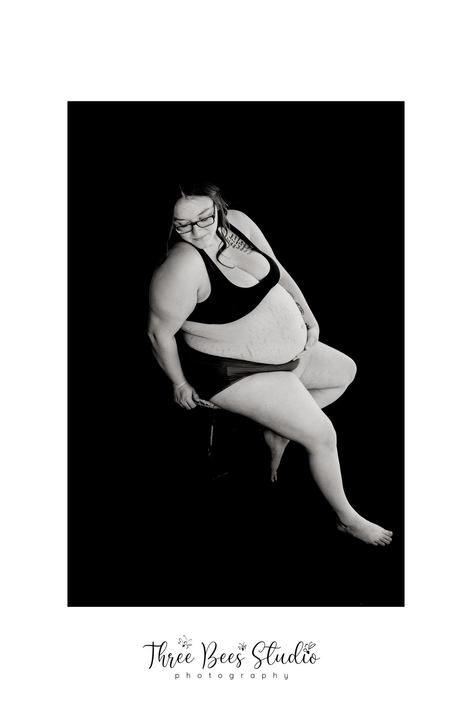Black and white artistic boudoir photo of a plus size person in dark clothing.