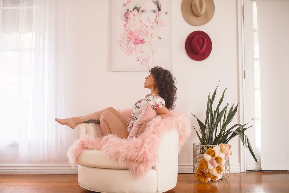 Person relaxing in pink armchair near potted plant and decorative wall art.
