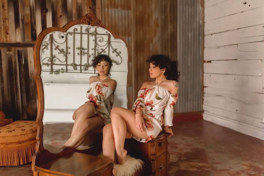 A person sitting in front of a mirror in artistic poses on vintage  furniture.