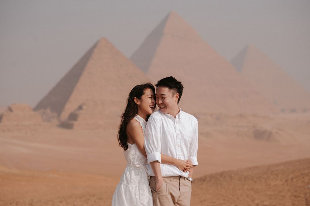 A romantic moment between a couple in white attire with the ancient pyramids of Giza in the background.