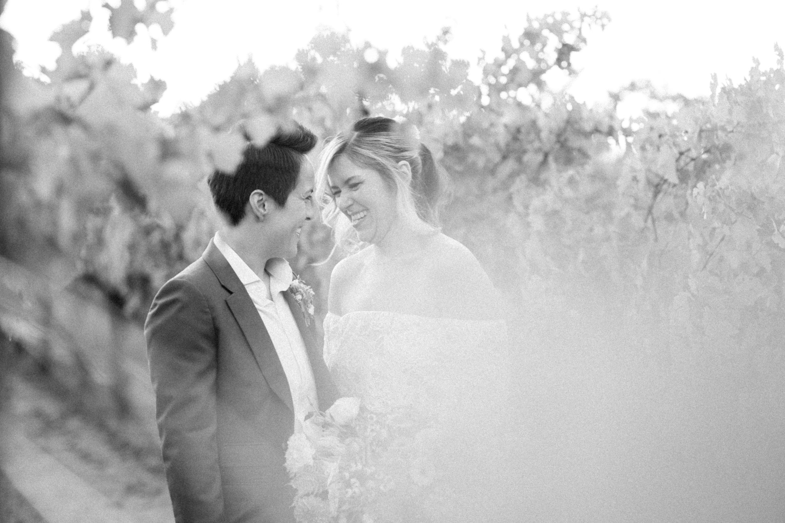Black and white photo of a smiling bride and groom sharing an intimate moment in a vineyard.