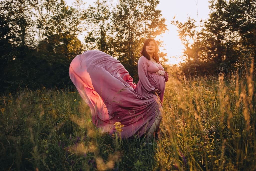 Figure in flowing pink dress twirling in golden sunset meadow with tall grass.