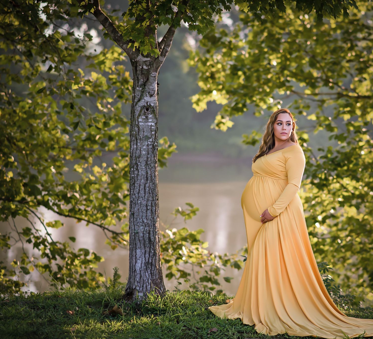 Ethereal maternity portrait in yellow dress beneath sunlit tree branches.