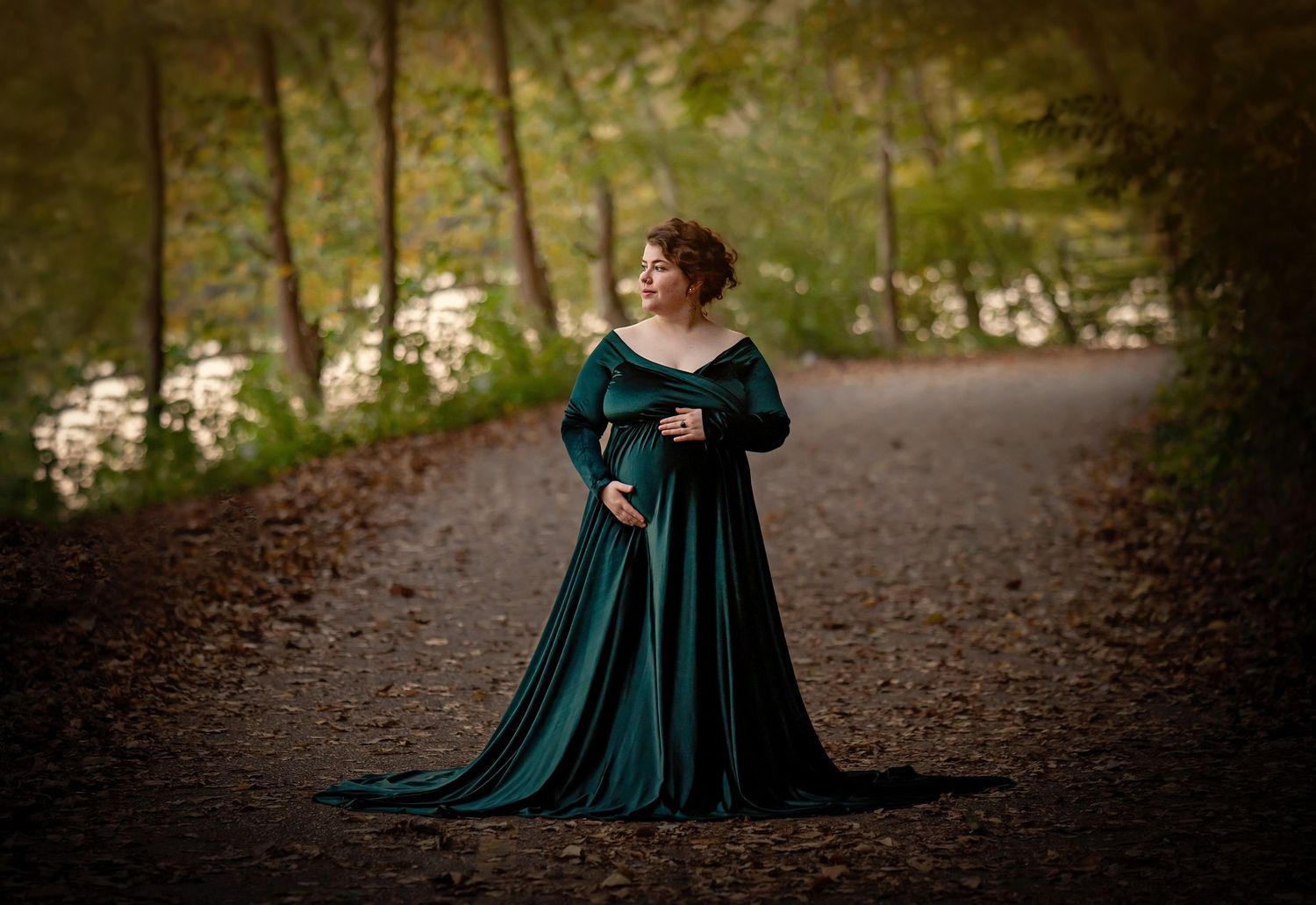 Dramatic maternity portrait in an emerald velvet gown on a forest path.