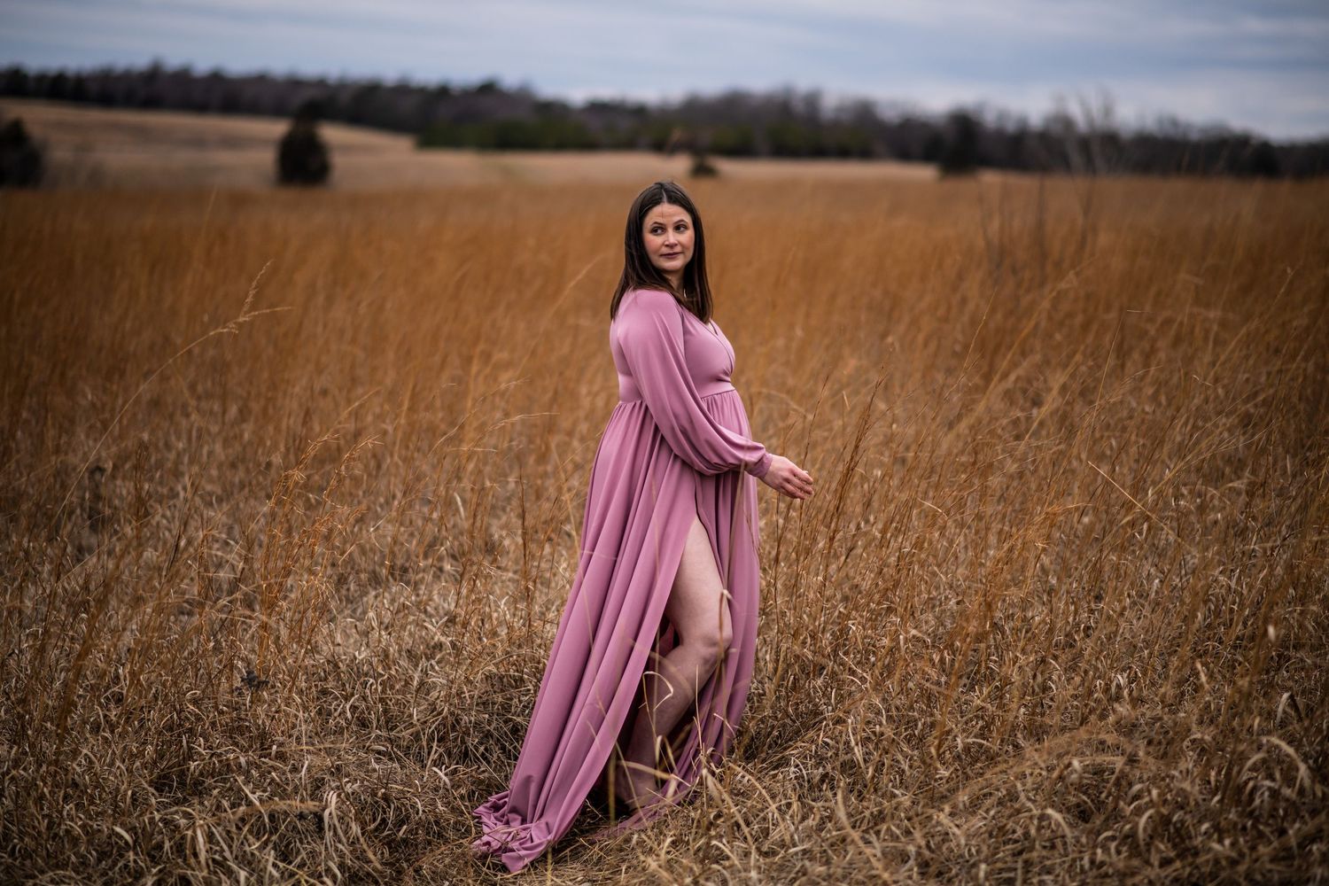 Dreamy portrait in dusty rose dress standing in golden autumn field.