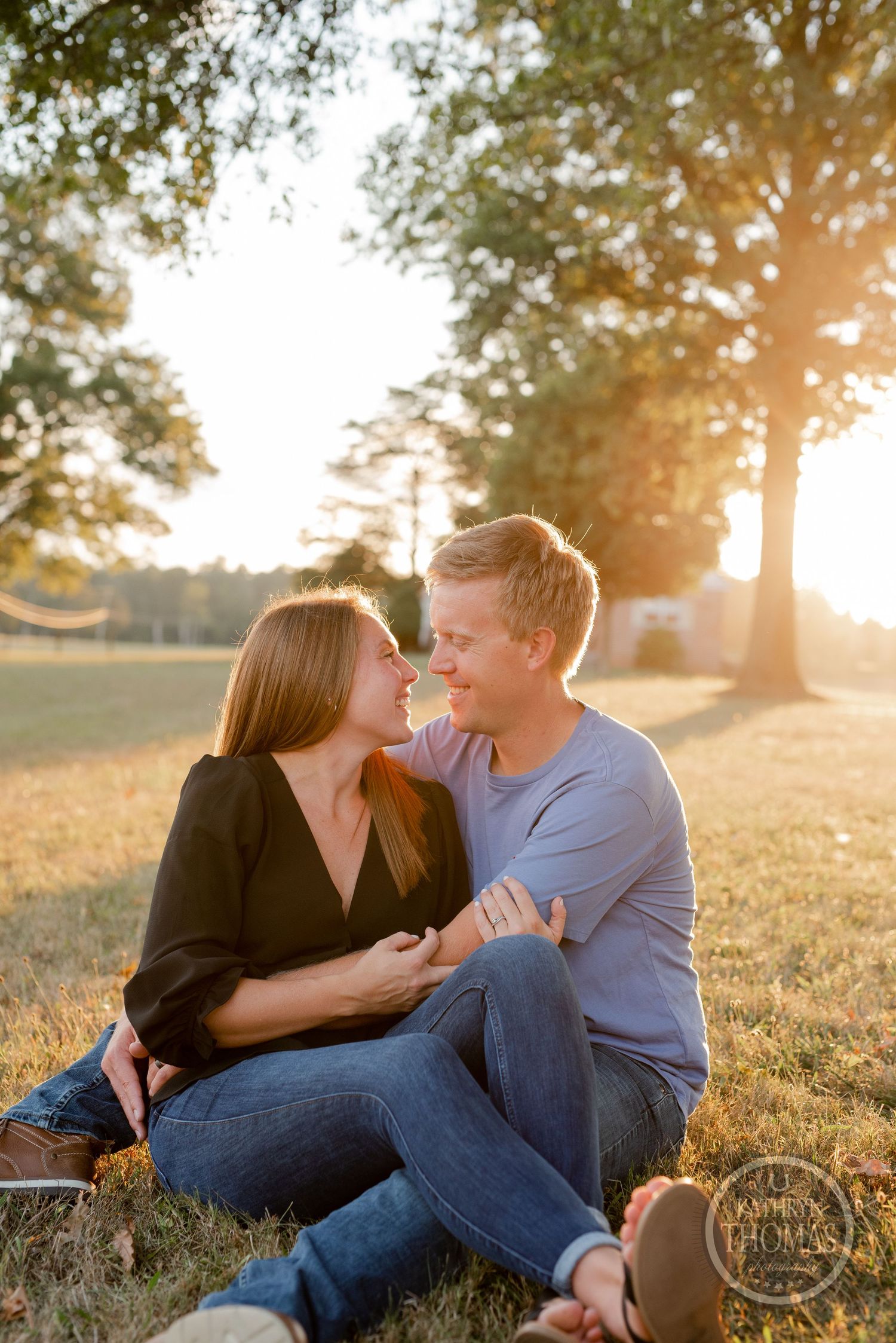 Couple sharing intimate moment while sitting in grass during golden hour.